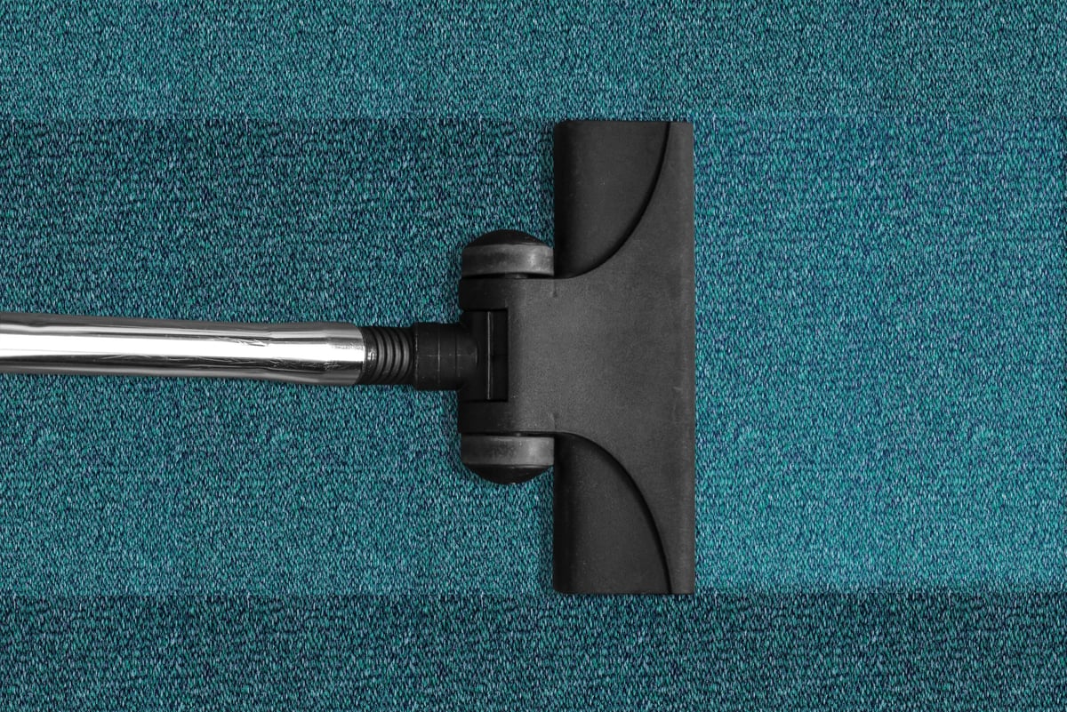 Vacuum cleaner nozzle with metal pipe on teal carpet, viewed from above