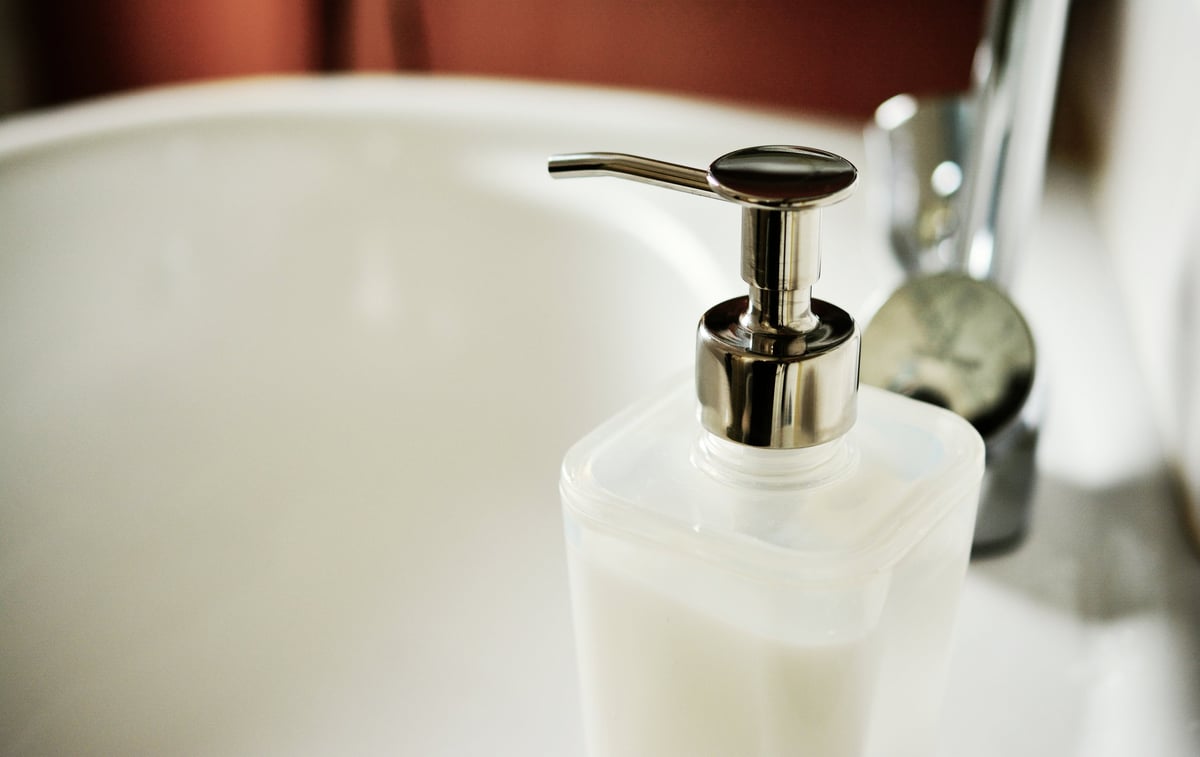 White soap dispenser with chrome pump next to bathroom sink